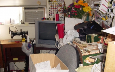 A television area with piles of trash and more supplies stacked around the room.