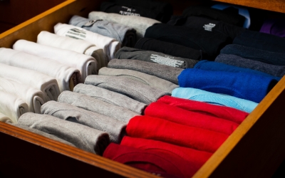 T-shirts folded and rolled neatly in a drawer with colors in their own groups.